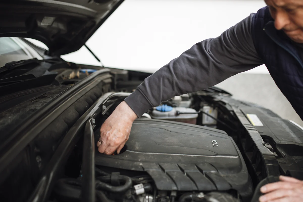 Personne penchée sur le compartiment moteur d'une voiture, capot ouvert, en train de contrôler les pièces